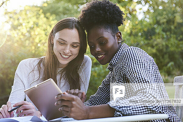 Lächelnde junge Freunde  die ein digitales Tablet benutzen  während sie im Park lernen  Orgeval