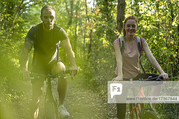 Lächelndes junges Paar beim Radfahren im Wald