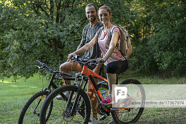 Portrait of smiling young couple sitting on bicycles in forest