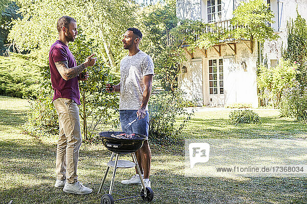 Young men with beer bottles talking near barbecue grill