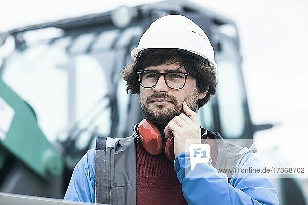 Junger Ingenieur mit Helm und Hörschutz checkt mit Laptop Arbeitstelle außen  Freiburg  Baden-Württemberg  Deutschland  Europa