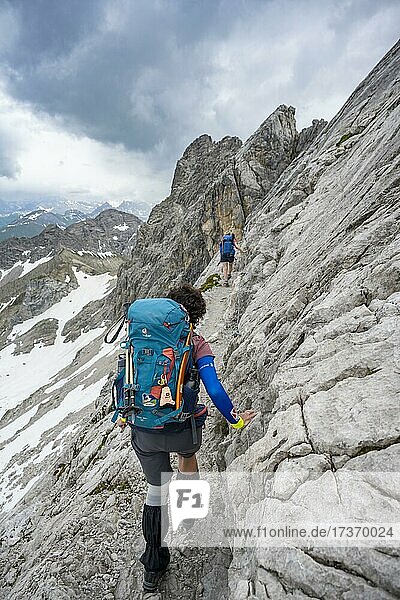 Wanderin  Bergsteigerin auf einem Gratweg mit Schneeresten  Bergpanorama mit Gipfel Hohes Licht  dramatischer Wolkenhimmel  Heilbronner Weg  Allgäuer Alpen  Allgäu  Bayern  Deutschland  Europa