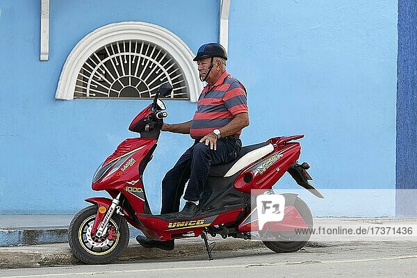 Mann  Kubaner auf Motorroller  rot  vor Haus  blau  Sancti Spiritus  Zentralkuba  Provinz Sancti Spiritus  Karibik  Kuba  Mittelamerika