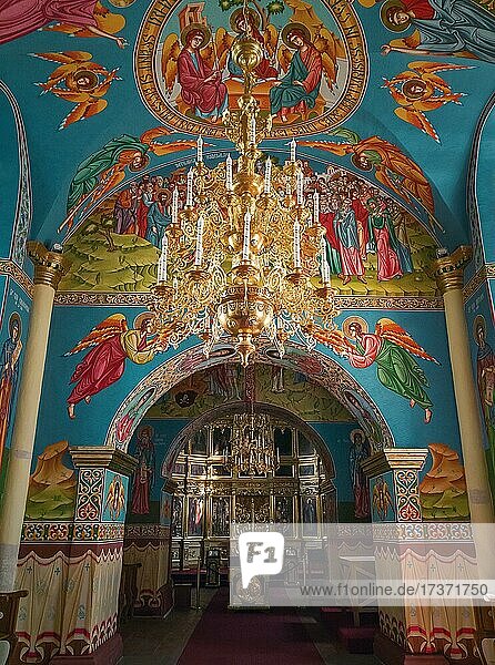 Wunderschön bemalte Wände und Decken im Inneren des Klosters Capriana  Moldawien. Goldener Kronleuchter  der mit leuchtenden Lichtern behängt ist. Verschiedene Ikonen von Heiligen  wie sie für christlich-orthodoxe Kirchen üblich sind