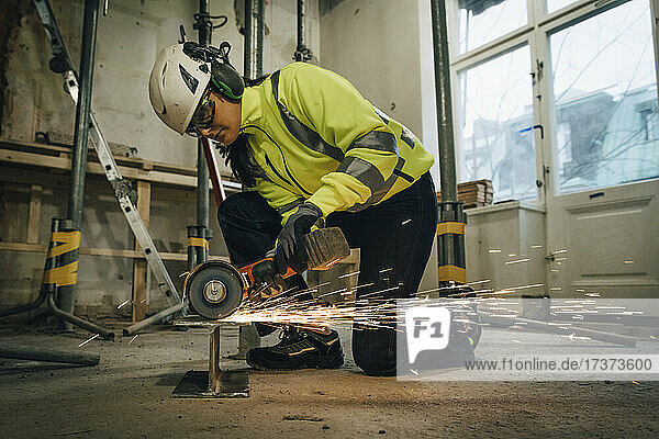 Bauarbeiterin in voller Länge beim Schneiden von Metall mit einer elektrischen Säge auf der Baustelle