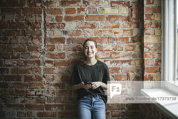 Lächelnder junger weiblicher Hacker mit Smartphone im Büro