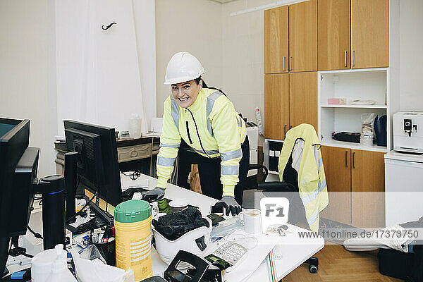 Porträt einer lächelnden Bauunternehmerin  die sich auf einen Schreibtisch im Büro stützt