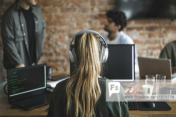 Weiblicher Hacker mit Kopfhörern bei der Arbeit am Computer im Büro