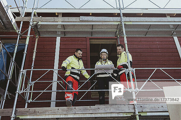 Weibliche Bauunternehmerin diskutiert mit männlichen Kollegen auf einem Baugerüst über einen Grundriss