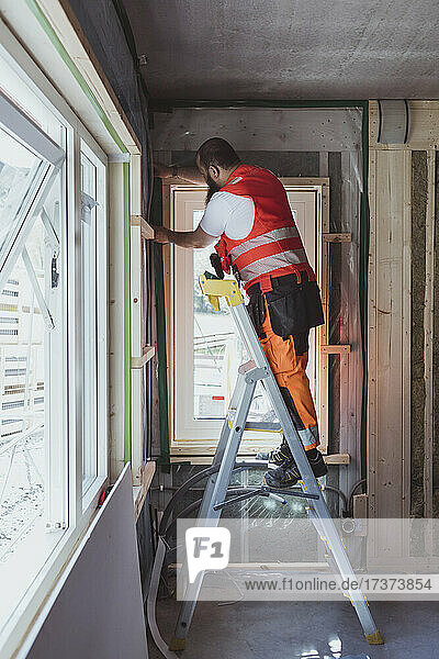 Full length of male construction worker standing on step ladder working at site