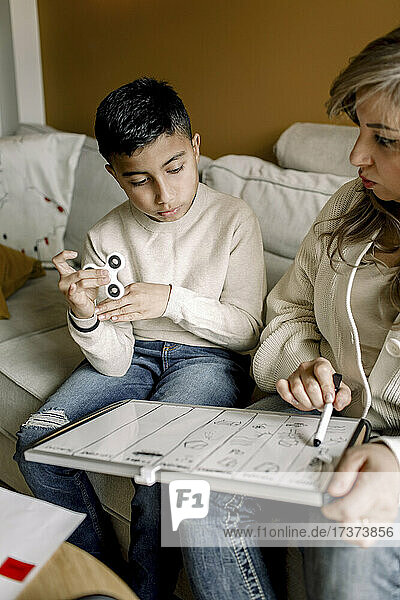 Mutter unterrichtet autistischen Jungen  während er auf dem Sofa im Wohnzimmer sitzt