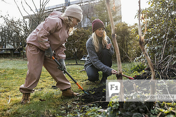 Mutter und Tochter graben in voller Länge mit einer Schaufel bei der Gartenarbeit im Hinterhof