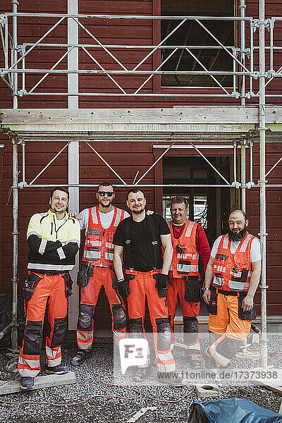 Männliche Bauarbeiter stehen auf der Baustelle in voller Länge zusammen