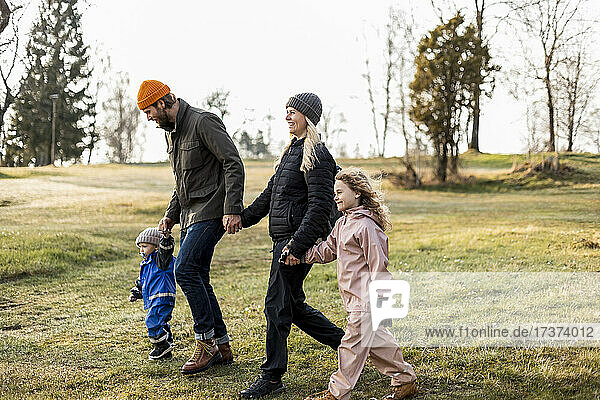 Glückliche Familie in voller Länge  die sich beim gemeinsamen Spaziergang im Park an den Händen hält