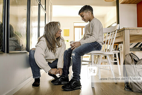 Mutter bindet den Schnürsenkel ihres autistischen Sohnes  der auf einem Stuhl im Wohnzimmer sitzt