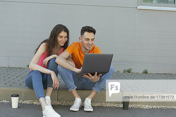 Junges Paar benutzt Laptop auf Bordsteinkante
