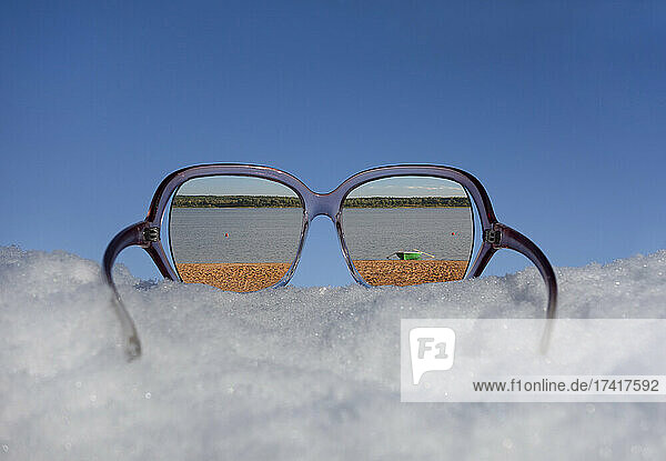 Strand und Seeufer in der Reflexion in der Sonnenbrille auf dichtem Schnee gesehen.