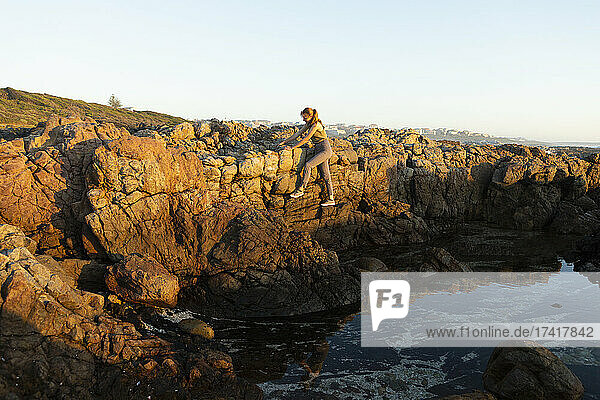Teenage girl climbing the rocks above a rockpool on the coast at De Kelders.