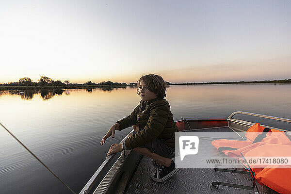A young boy fishing from a boat on the flat calm waters of the Okavango Delta at sunset