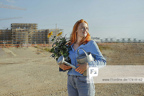 Woman carrying potted plant and watering can at construction site
