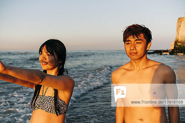 Male and female friends looking away while standing at beach during sunset