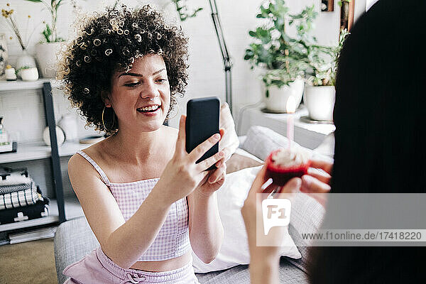 Lächelnde Frau fotografiert Freundin zu Hause per Smartphone
