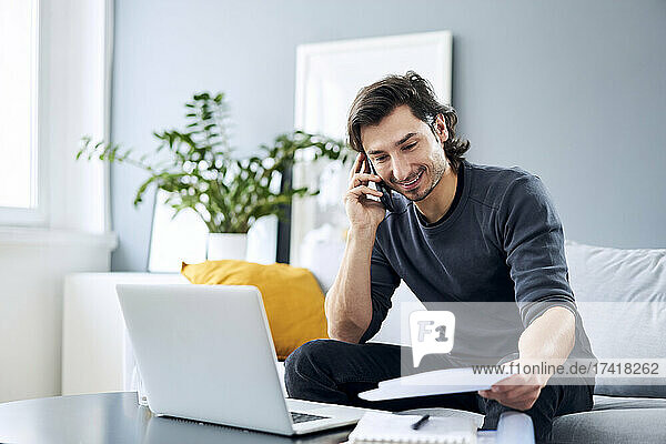 Male professional talking on smart phone while holding document at home