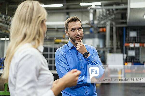 Thoughtful businessman with hand on chin standing by colleague in factory