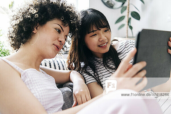 Smiling woman using digital tablet with female friend at home