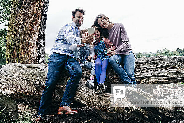 Vater macht Selfie per Smartphone  während er mit der Familie auf einem umgestürzten Baum sitzt