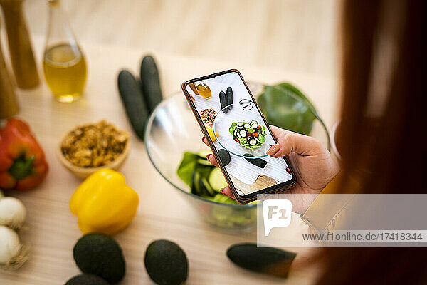Frau fotografiert Salatschüssel mit Handy am Tisch
