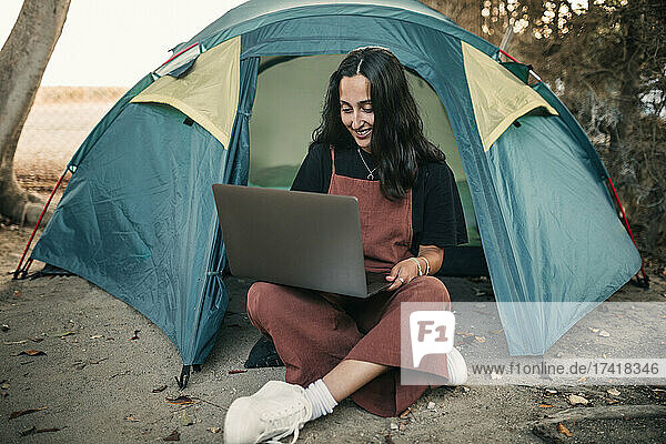 Lächelnde Freiberuflerin  die am Wochenende im Zelt sitzt und am Laptop arbeitet