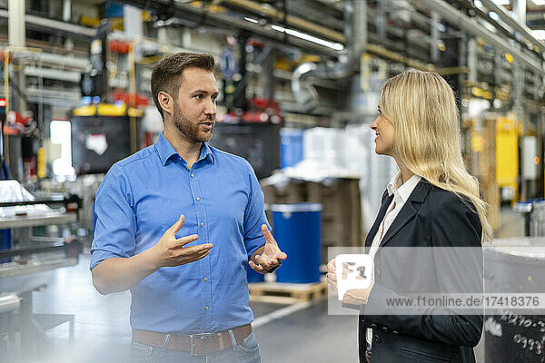 Male professional discussing with female coworker at factory