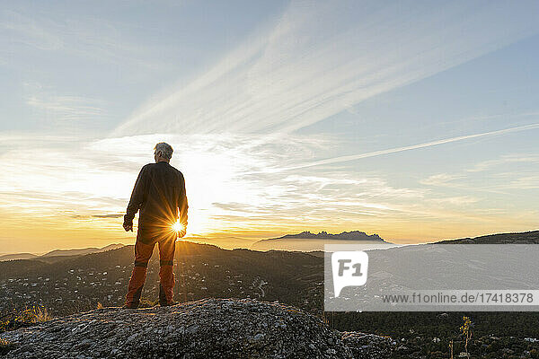 Man standing on cliff while looking at mountain