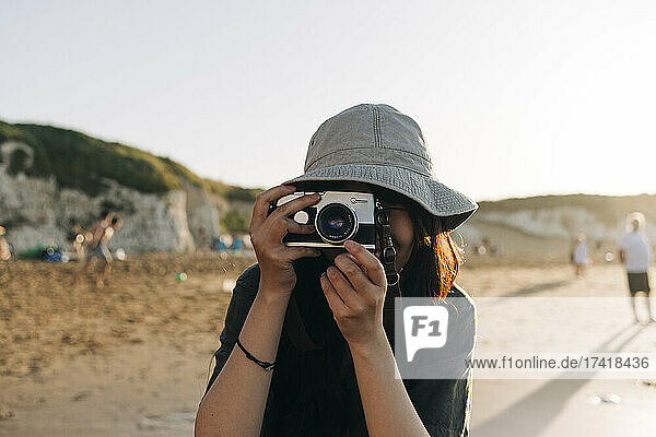 Young woman photographing through camera at beach