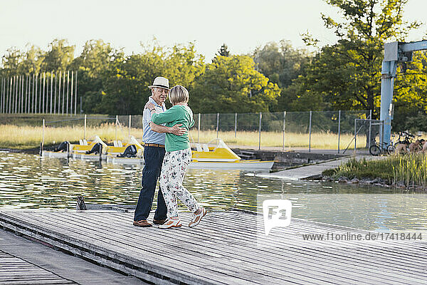 Happy senior couple dancing on jetty by lake