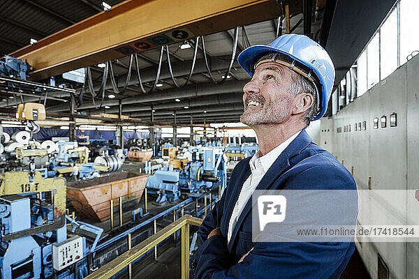 Smiling male engineer with hardhat looking at overhead crane in steel mill