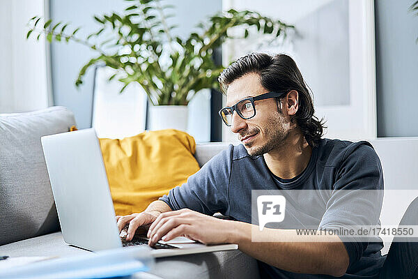 Male student with eyeglasses using laptop at home