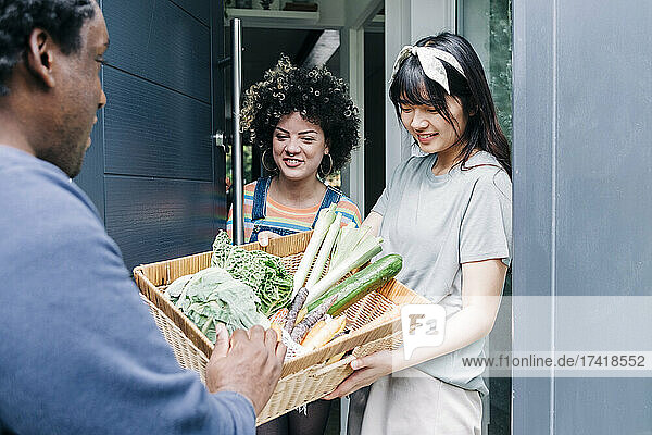 Delivery man giving fresh vegetable basket to women at doorway