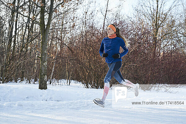 Young woman jogging near bare trees during snow in winter