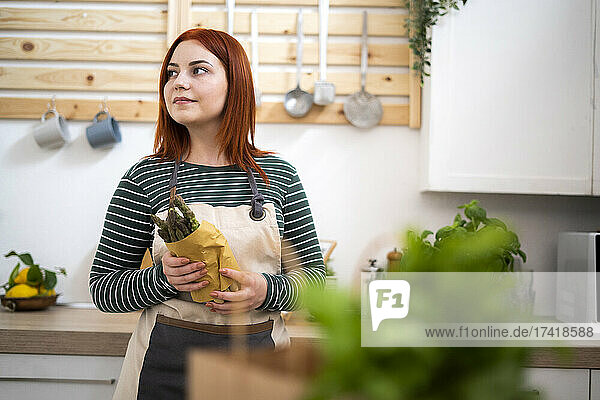 Thoughtful woman holding asparagus while standing in kitchen