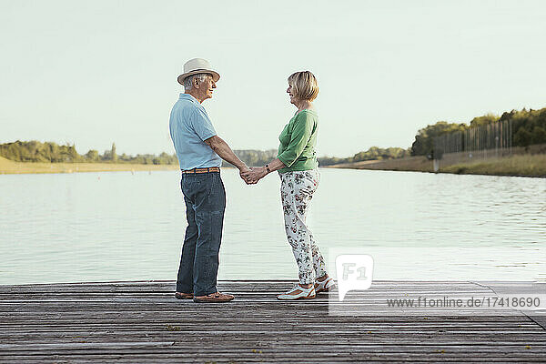 Senior couple holding hands while standing on jetty by lake