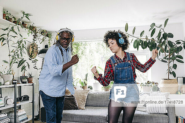 Young woman listening music through headphones while dancing with father at home