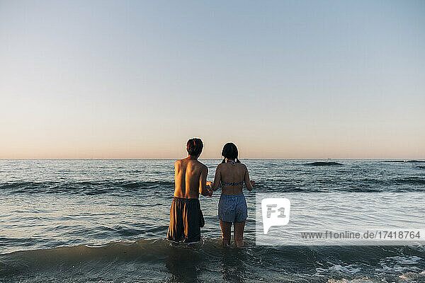 Young male and female friends looking at sea during sunset
