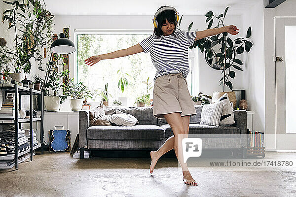 Carefree woman with arms outstretched dancing at home