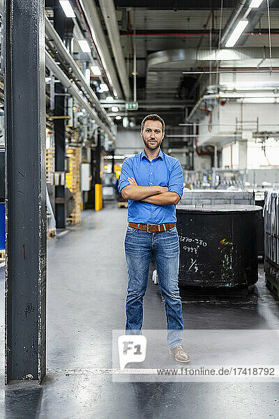 Confident businessman with arms crossed standing at factory