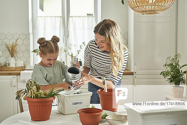 Mother and daughter watering homemade compost in container on table