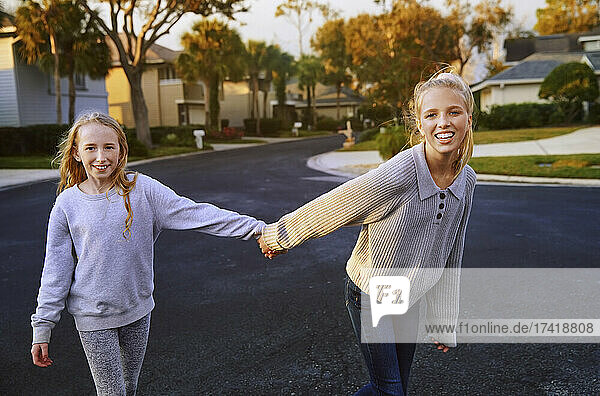 Smiling girls holding hands while walking on road