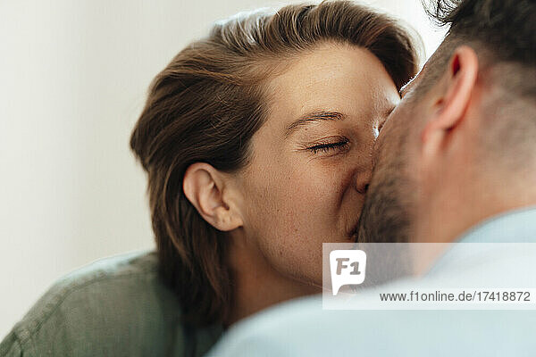 Woman with eyes closed kissing man at home