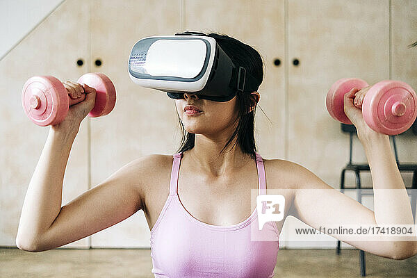 Frau benutzt Virtual-Reality-Headset  während sie zu Hause Hanteln hält